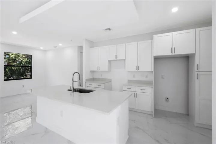 Kitchen with white cabinets, recessed lighting, light marble finish flooring, a center island with sink, and light stone counters