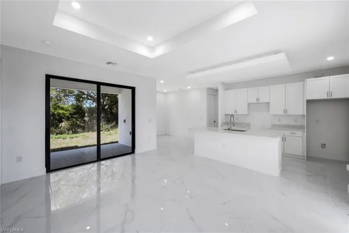 Kitchen with white cabinets, a raised ceiling, recessed lighting, a kitchen island with sink, and open floor plan