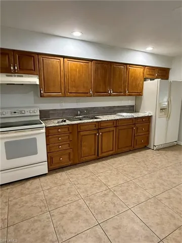 Kitchen featuring white appliances, brown cabinetry, under cabinet range hood, light tile patterned flooring, and recessed lighting