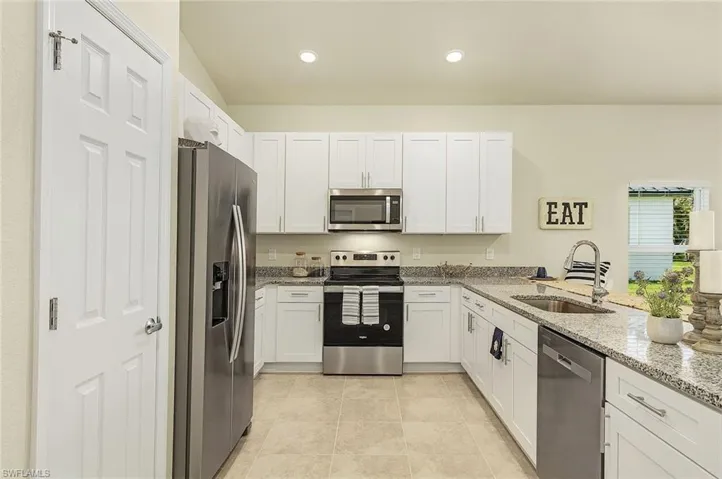 Kitchen with light stone countertops, stainless steel appliances, white cabinets, recessed lighting, and light tile patterned flooring