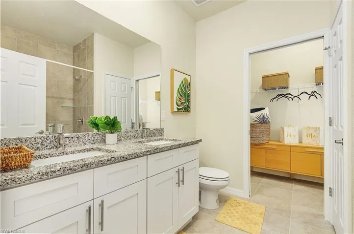 Bathroom featuring a walk in closet, double vanity, a shower stall, and light tile patterned flooring