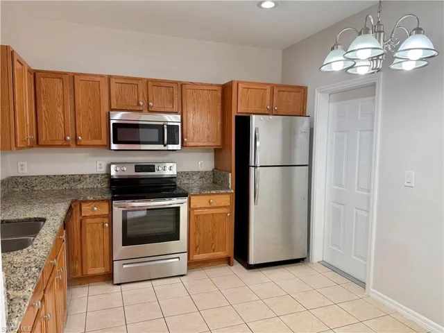 Kitchen with dark stone counters, appliances with stainless steel finishes, brown cabinets, light tile patterned floors, and a chandelier
