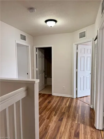 Corridor featuring light wood-style flooring, a textured ceiling, and an upstairs landing