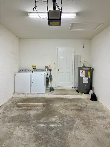 Garage featuring a textured wall, separate washer and dryer, electric water heater, and a garage door opener