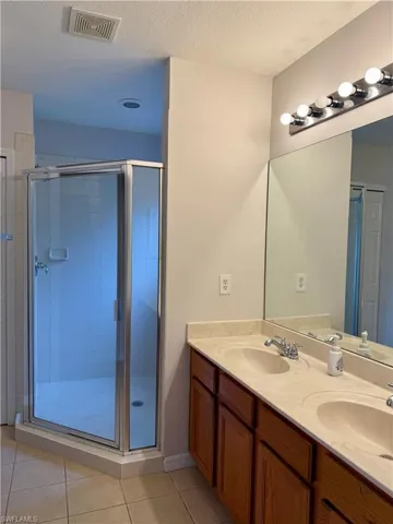 Bathroom featuring double vanity, a stall shower, a textured ceiling, and light tile patterned floors