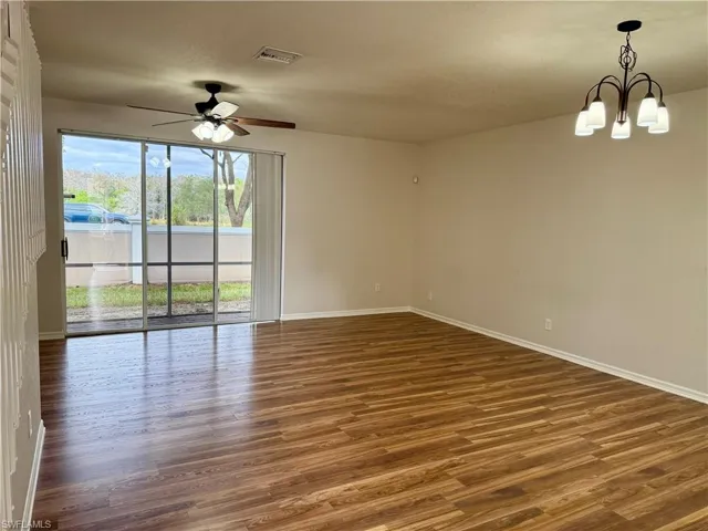 Empty room with dark wood-style floors, a chandelier, and ceiling fan