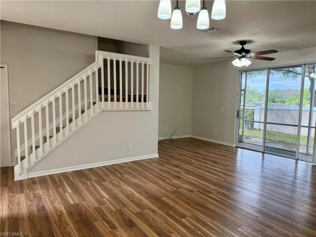Unfurnished living room featuring dark wood-style floors, stairway, ceiling fan, and a chandelier