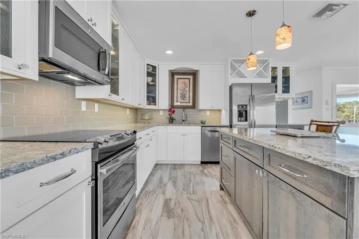 Kitchen with glass insert cabinets, stainless steel appliances, decorative light fixtures, white cabinets, and recessed lighting