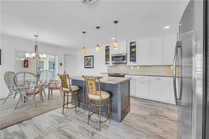 Kitchen featuring appliances with stainless steel finishes, white cabinets, a kitchen breakfast bar, light stone counters, and pendant lighting