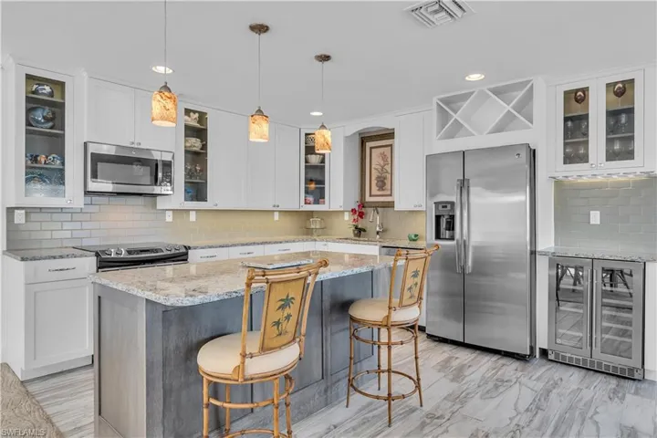 Kitchen featuring glass insert cabinets, appliances with stainless steel finishes, wine cooler, light stone countertops, and tasteful backsplash