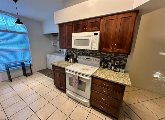 Kitchen with white appliances, light stone counters, light tile patterned flooring, dark brown cabinets, and tasteful backsplash