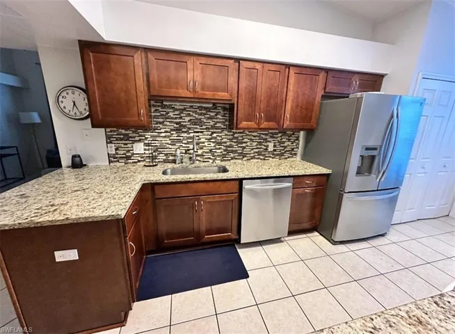 Kitchen featuring tasteful backsplash, light stone countertops, light tile patterned flooring, appliances with stainless steel finishes, and vaulted ceiling
