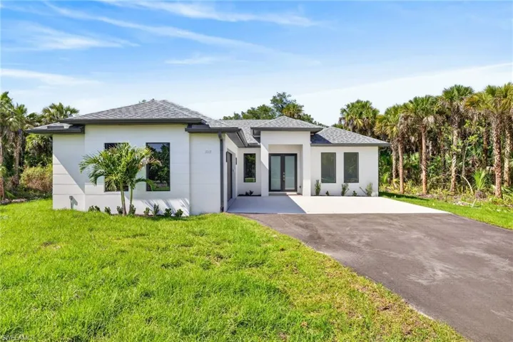 Contemporary single-story exterior featuring a white stucco facade, gray shingled hip roof, covered entryway, and asphalt driveway