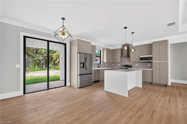 Kitchen featuring flat-panel cabinetry, a quartz-topped waterfall island, stainless steel appliances, patterned backsplash tile, and wood-finish flooring