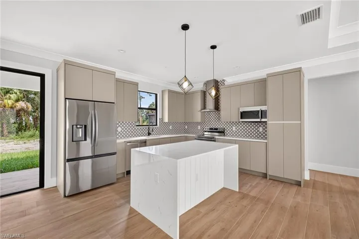 Kitchen featuring flat-panel cabinetry, a quartz-topped waterfall island, geometric patterned backsplash, stainless steel appliances, and wood-finish flooring