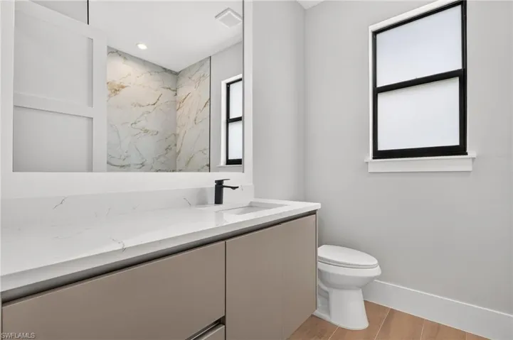 Flat-panel cabinetry with a quartz countertop, integrated rectangular sink, matte black faucet, and wood-finish flooring