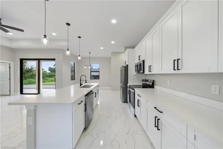 Kitchen with appliances with stainless steel finishes, a ceiling fan, light countertops, white cabinets, and an island with sink
