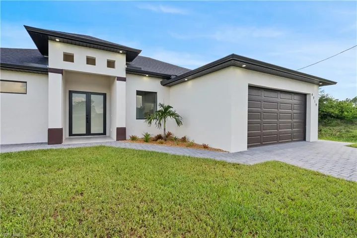 View of front of home with an attached garage, stucco siding, driveway, a front lawn, and french doors