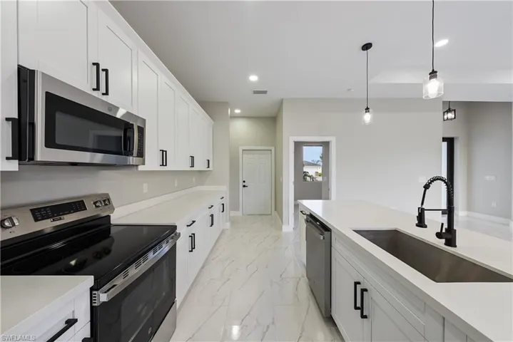 Kitchen featuring stainless steel appliances, light marble finish flooring, recessed lighting, decorative light fixtures, and white cabinets