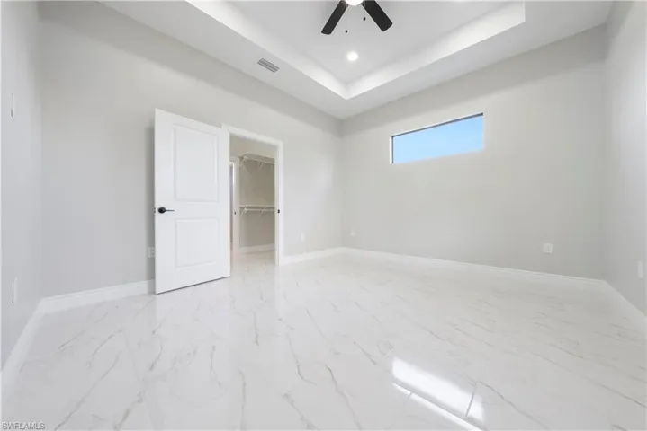 Unfurnished bedroom featuring light marble finish floors, a raised ceiling, a spacious closet, ceiling fan, and recessed lighting