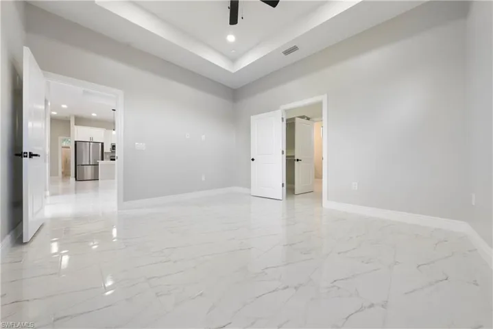 Empty room with light marble finish floors, recessed lighting, ceiling fan, a raised ceiling, and a high ceiling