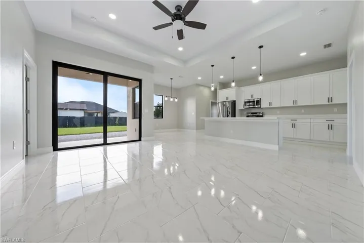 Unfurnished living room featuring a tray ceiling, light marble finish flooring, a ceiling fan, and recessed lighting