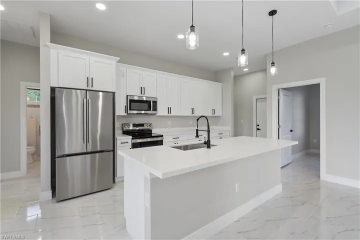 Kitchen with light marble finish flooring, appliances with stainless steel finishes, recessed lighting, and white cabinets
