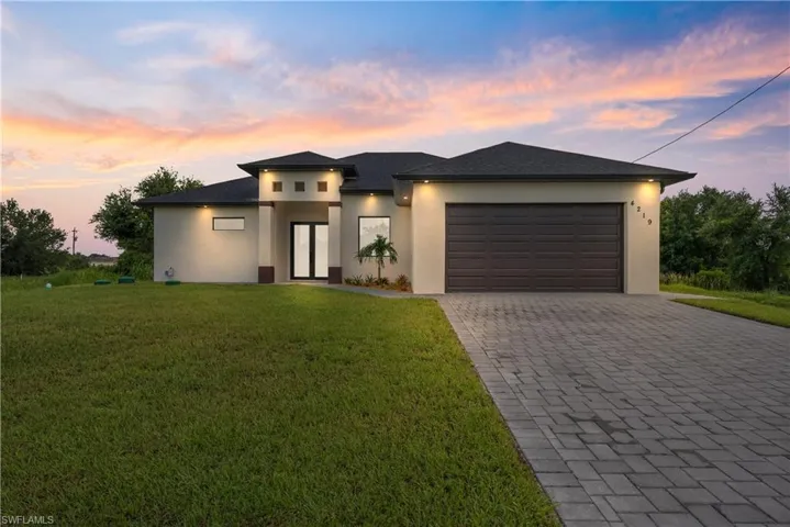 Prairie-style house featuring stucco siding, a garage, decorative driveway, and a lawn