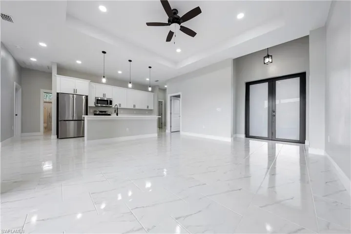 Unfurnished living room with a tray ceiling, light marble finish floors, recessed lighting, french doors, and a ceiling fan