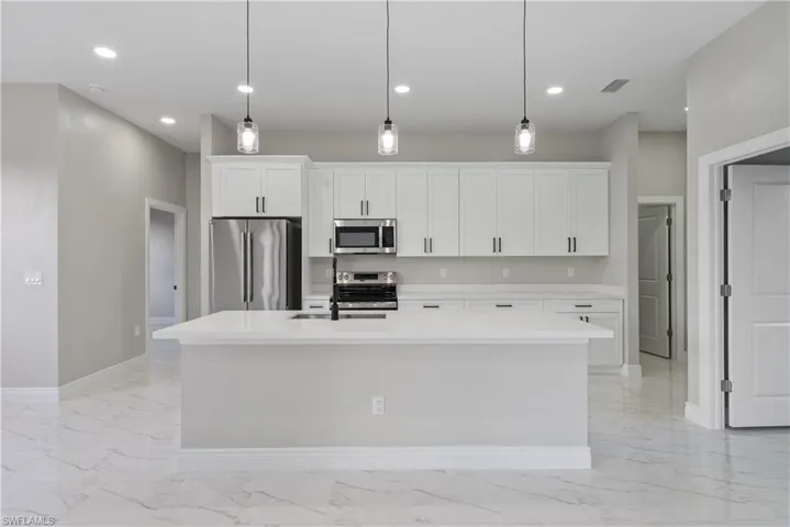 Kitchen featuring appliances with stainless steel finishes, an island with sink, white cabinetry, light countertops, and recessed lighting