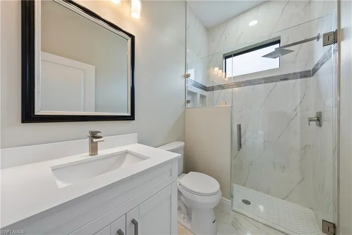 Bathroom featuring vanity, a marble finish shower, and marble look tile flooring