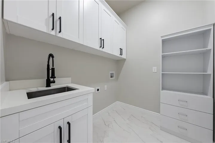 Laundry area with hookup for an electric dryer, hookup for a washing machine, light marble finish flooring, and cabinet space