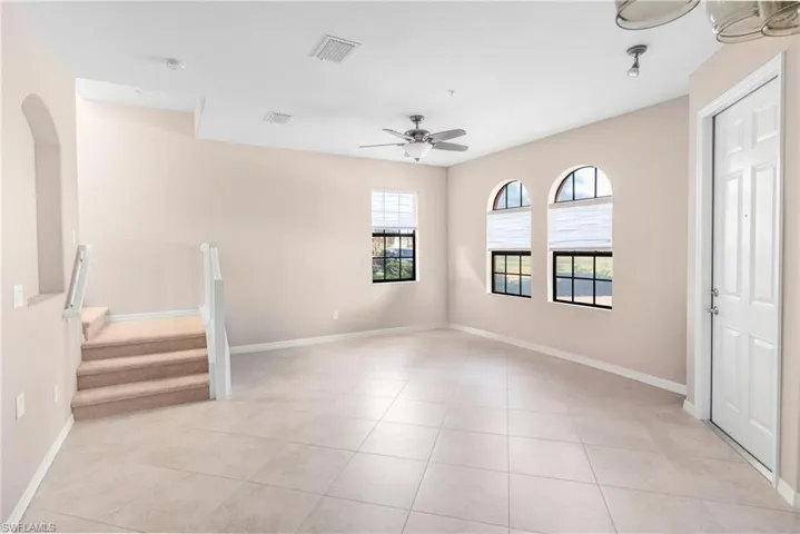 Empty room with a ceiling fan, stairs, and light tile patterned flooring