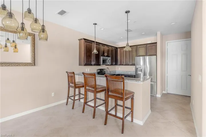Kitchen featuring a peninsula, decorative light fixtures, dark brown cabinets, a kitchen breakfast bar, and appliances with stainless steel finishes