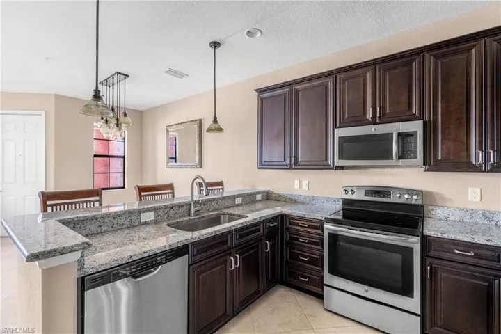 Kitchen featuring stainless steel appliances, a kitchen bar, light stone countertops, dark brown cabinets, and a textured ceiling