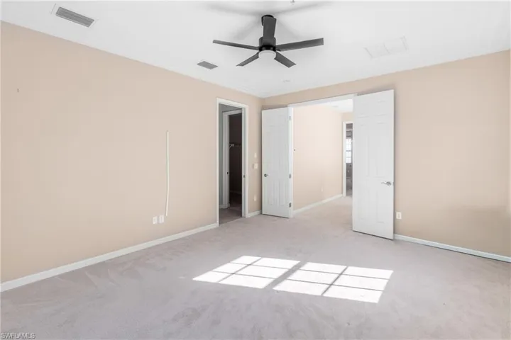 Unfurnished bedroom featuring a ceiling fan, light carpet, crown molding, and a walk in closet