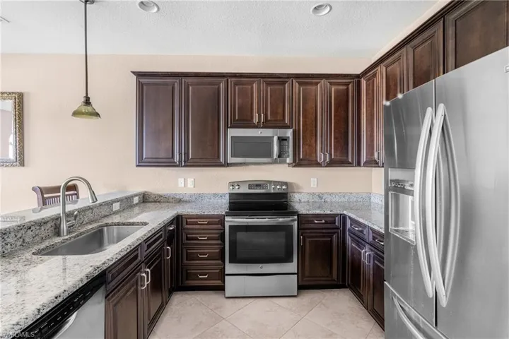 Kitchen with stainless steel appliances, light stone countertops, dark brown cabinets, a textured ceiling, and recessed lighting