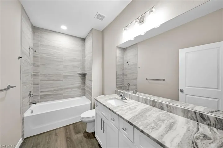 Full bathroom with hardwood / wood-style floors, tiled shower / bath combo, toilet, and vanity