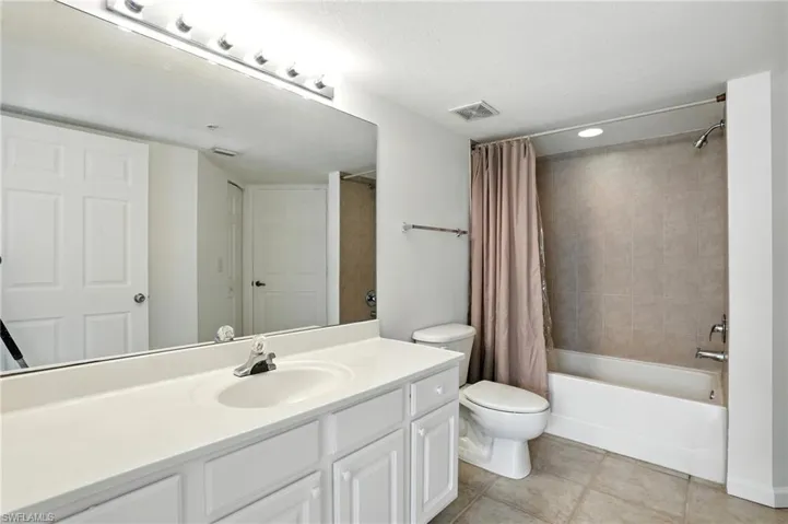 Bathroom with shower / tub combo with curtain, vanity, light tile patterned floors, and a textured ceiling