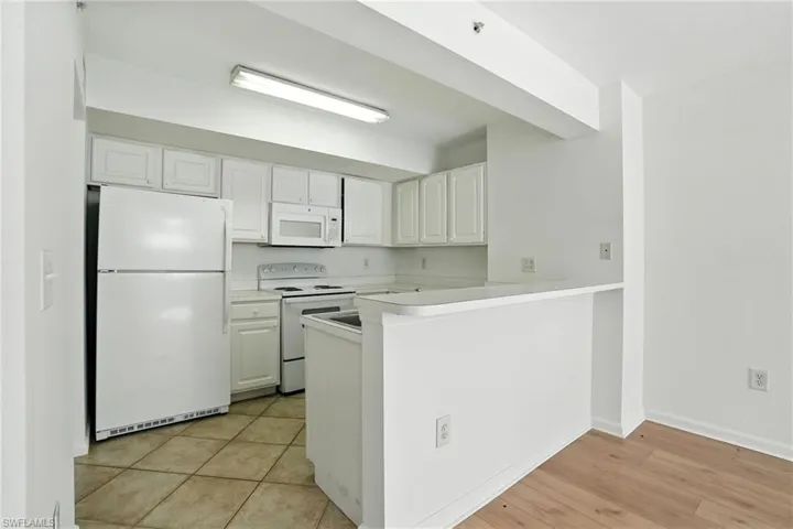 Kitchen with white appliances, white cabinetry, light countertops, and a peninsula