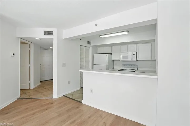Kitchen with white cabinetry, light wood-type flooring, light countertops, white appliances, and a peninsula