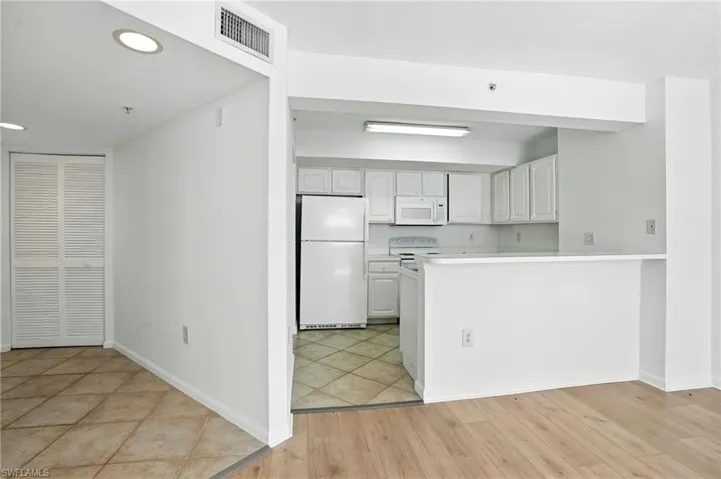 Kitchen with white appliances, white cabinets, light countertops, a peninsula, and light wood finished floors