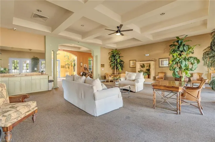 Living area with ornate columns, coffered ceiling, arched walkways, carpet flooring, and a ceiling fan