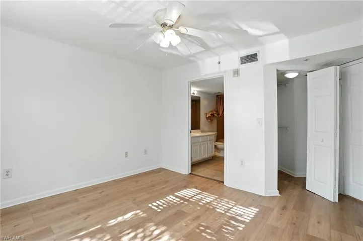 Unfurnished bedroom with light wood finished floors, connected bathroom, a ceiling fan, and a walk in closet