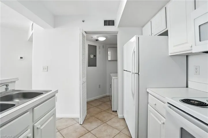 Kitchen featuring white cabinetry, light countertops, white appliances, light tile patterned floors, and electric panel