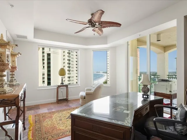 Office with a ceiling fan, stone tile floors, and a raised ceiling