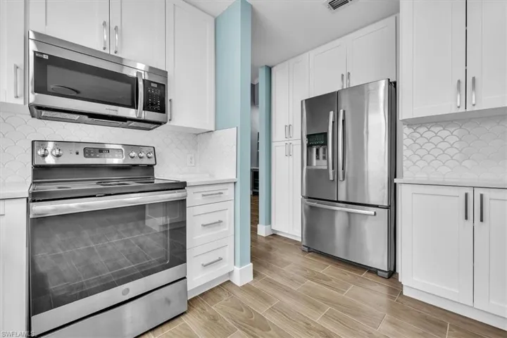 Modern kitchen featuring white shaker cabinetry, stainless steel appliances, a scalloped tile backsplash, light-toned countertops, and wood-finish flooring