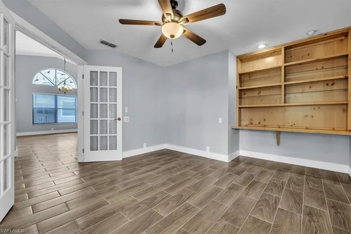 Room featuring wood-finish tile flooring, a ceiling fan with integrated lighting, and a built-in shelving unit with task lighting