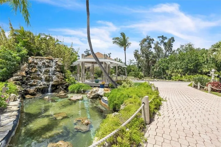 Manicured landscaping featuring a multi-tiered rock waterfall, a tranquil pond, and a spacious wooden gazebo