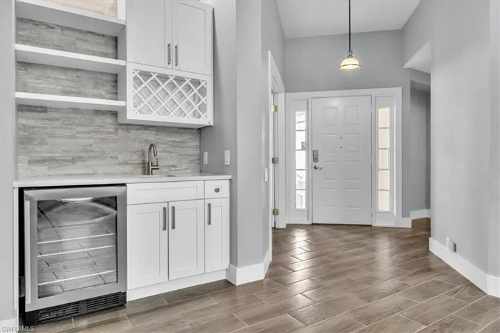 Foyer featuring wood-finish flooring, a white paneled entry door with sidelights, and a built-in wet bar with white cabinetry, a beverage refrigerator, and a tile backsplash